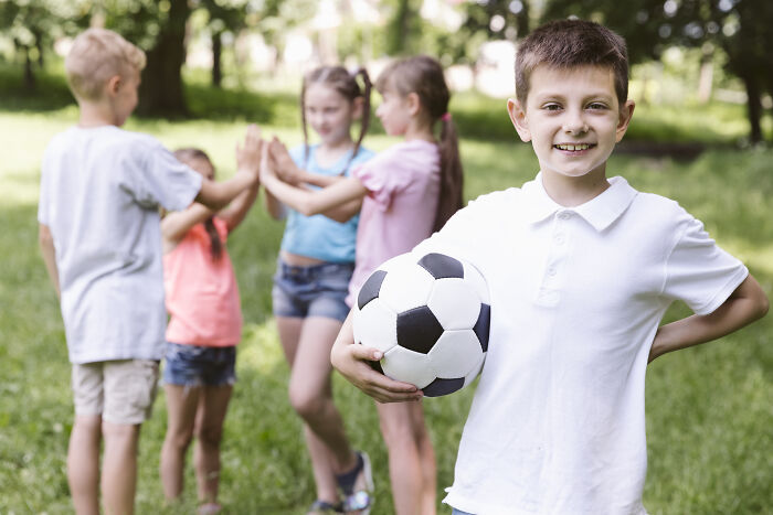 Boy holding a soccer ball at a birthday party in a grassy park.