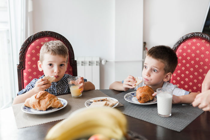 Two boys sitting at a table, eating breakfast with juice and milk, related to allergies and family concerns.
