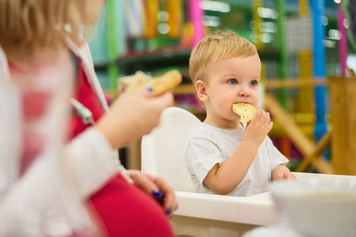 Toddler in a high chair eating bread, potential allergy concerns highlighted by father's question.