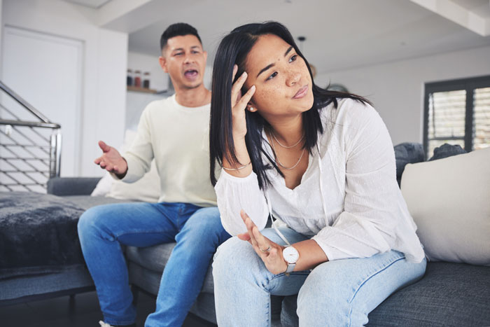 Man and woman having a serious discussion on a sofa, highlighting possible disregard for child allergies.