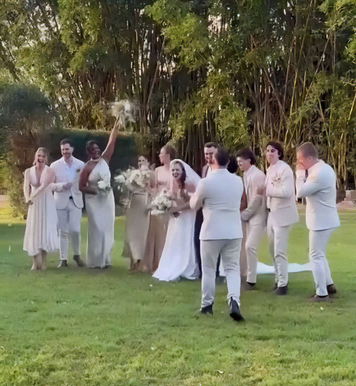 Wedding party joyfully celebrating miracle survivor's special day outdoors in elegant attire.