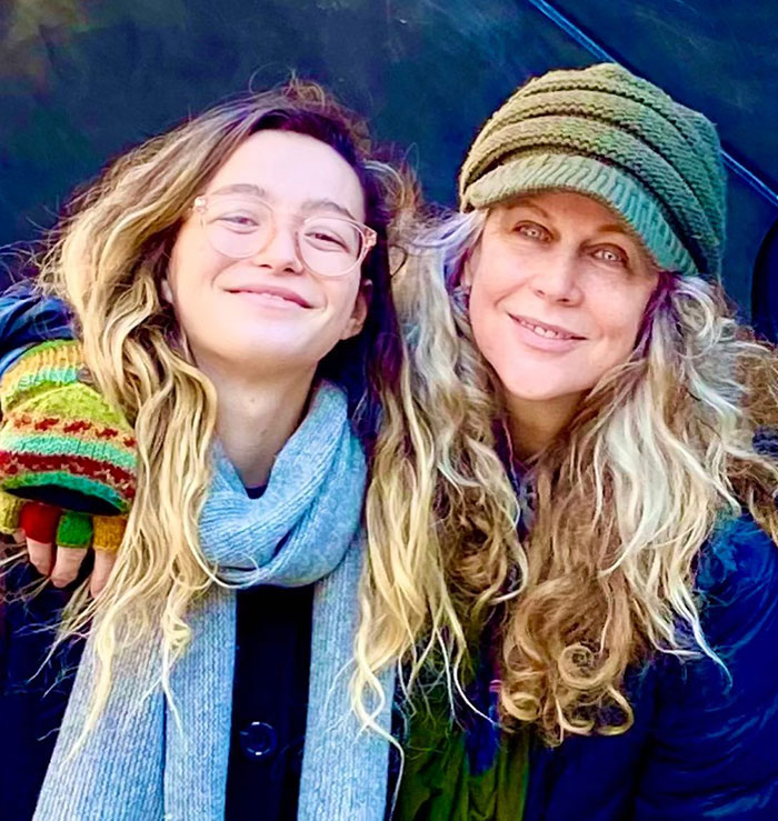 Two smiling women outdoors, one wearing glasses and a scarf, the other a green knit hat, highlighting child star Sophie Nyweide.