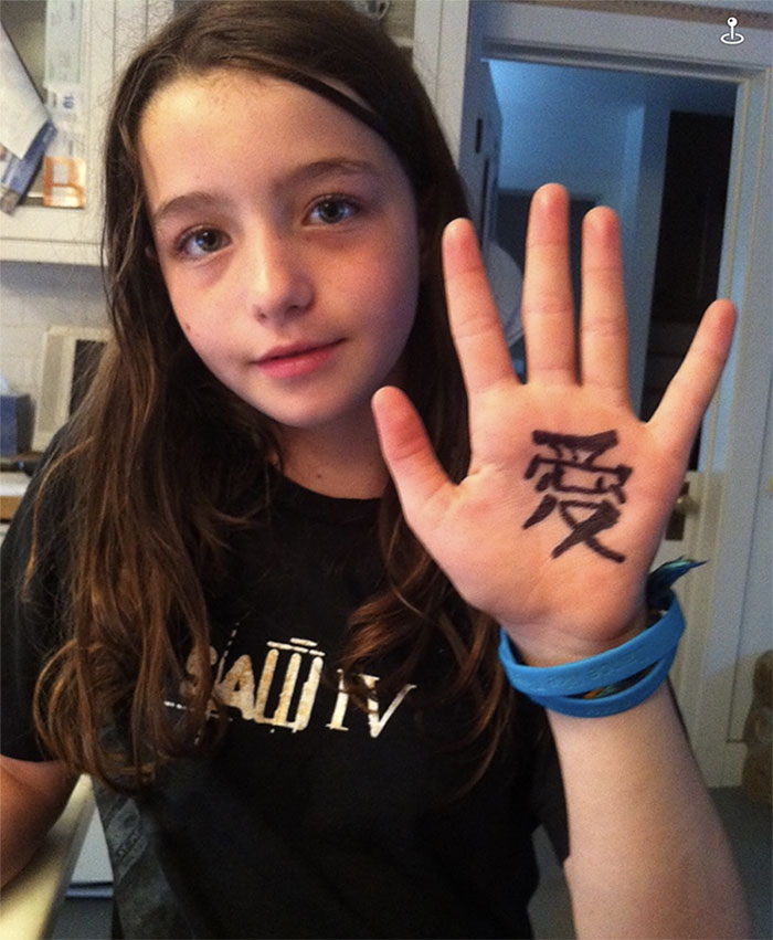 Young girl with long hair holding up hand with a symbol, in a casual setting; related to Child Star Sophie Nyweide.
