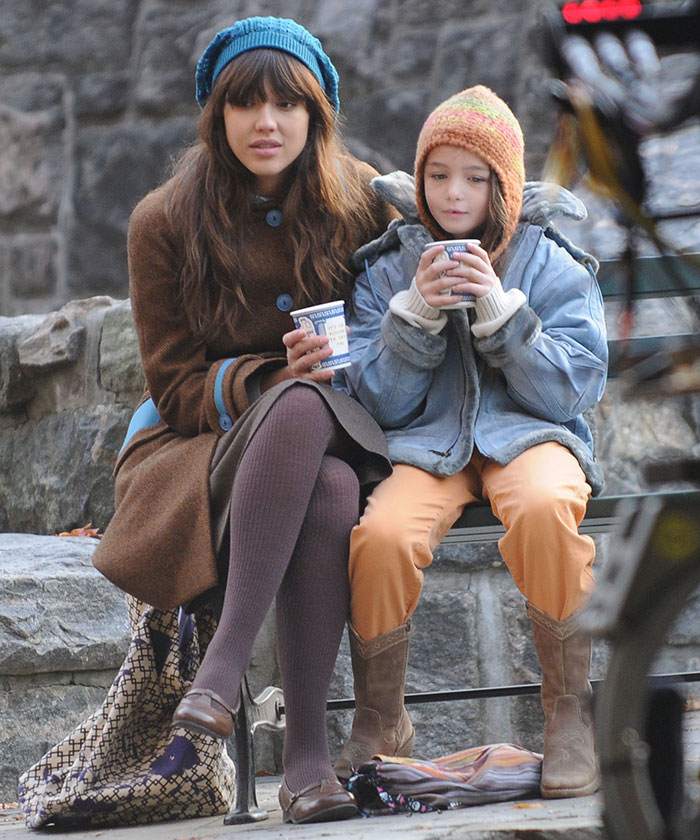 Two people sitting on a bench, wearing winter clothes, drinking from cups.