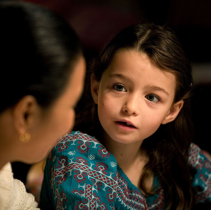 Former child star in a detailed blue dress, listening intently, with a curious expression.
