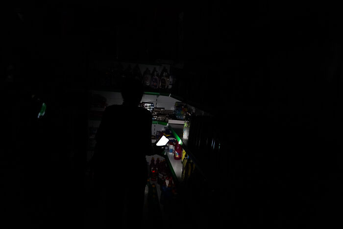 Person using a phone flashlight in a dark store during a major blackout affecting 50 million Europeans and paralyzing activities