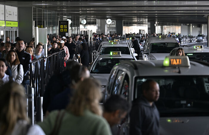 Crowded airport taxi queue with many people waiting, illustrating the impact of a major blackout paralyzing activities in Europe.