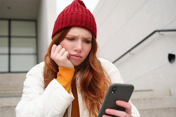 Woman in a red beanie looks at her phone, frustrated with spam caller issues.