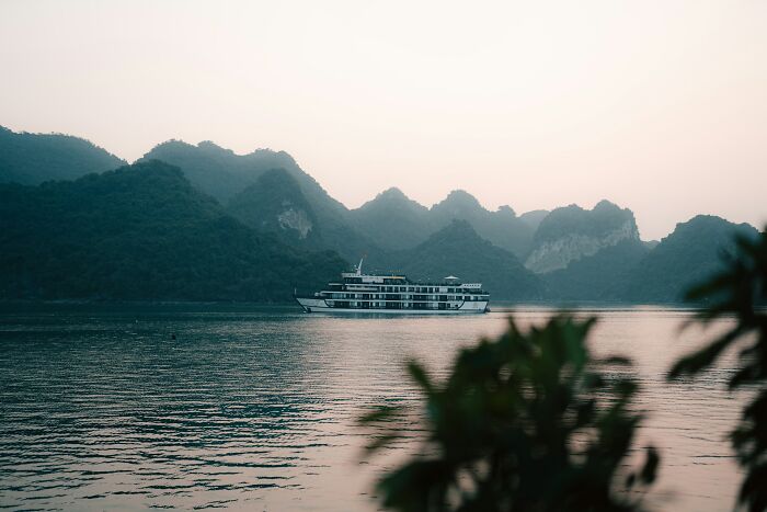 Luxury cruise ship sailing near lush island mountains at sunset.