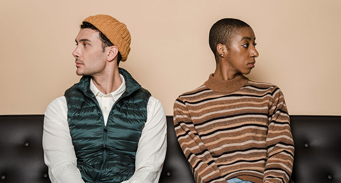 A couple sits on a couch, looking away from each other, reflecting tension over a dog-related decision.