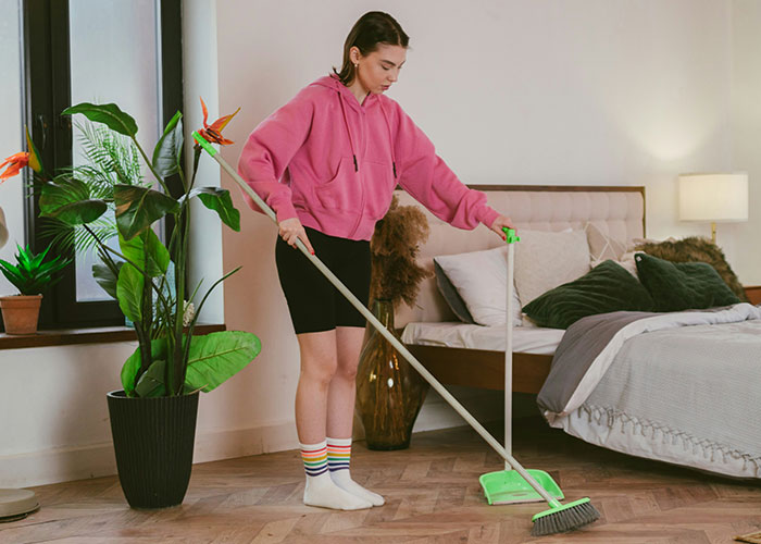 Stepdaughter in a pink hoodie cleaning her bedroom, illustrating household chores.