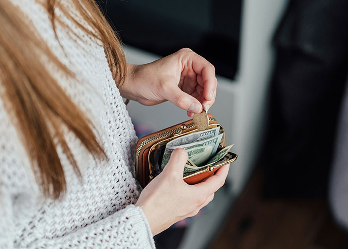 Woman in a knitted sweater handling cash and coins from a wallet, symbolizing overcharged rent.