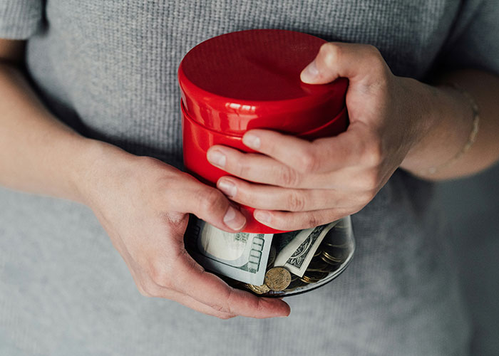 Person holding a jar with cash and coins, symbolizing overcharged rent for chores.