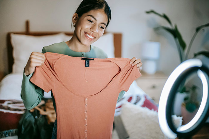 Young woman smiling and holding a dress under a ring light, suggests emotions tied to karma and personal stories.