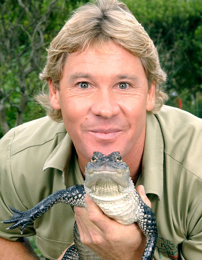 Steve Irwin holding a small crocodile and smiling, wearing a khaki shirt, in an outdoor setting.