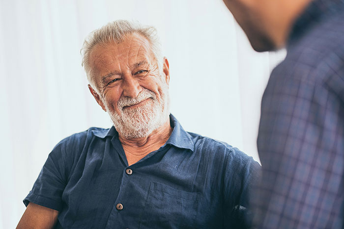 Elderly man smiling in conversation, wearing a blue shirt, discussing a casual admission.
