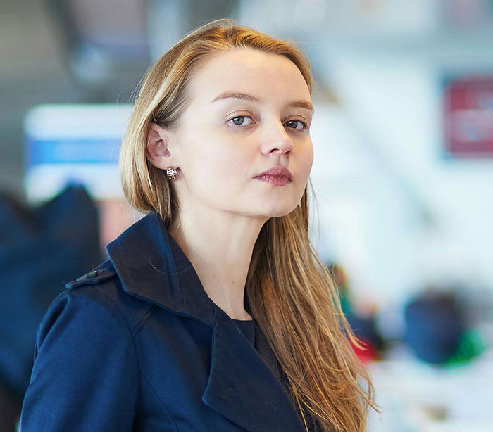 Young woman in a blue coat in a public setting, embodying casual confidence amidst crazy admissions.