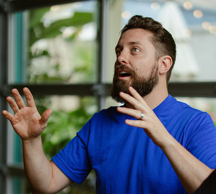 Man in a blue shirt gesturing animatedly, possibly sharing a crazy admission in conversation.