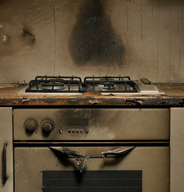 Burnt kitchen stove with charred knobs and a blackened oven door, highlighting an aftermath of a crazy incident.