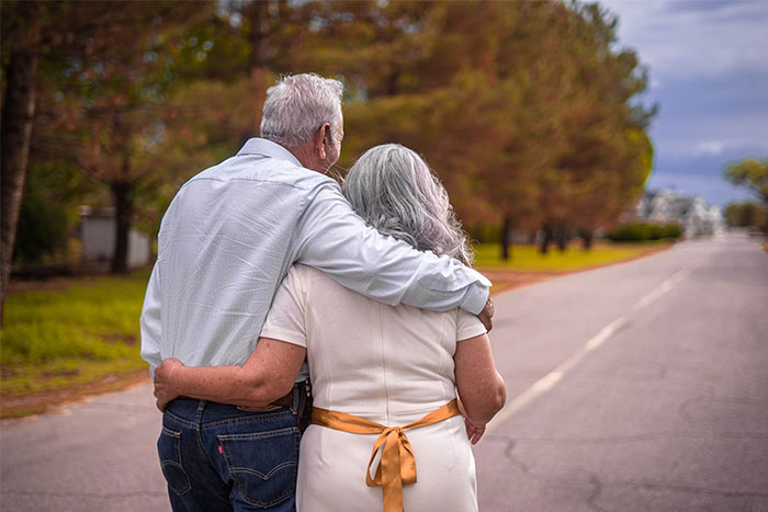 Elderly couple walking arm in arm down a tree-lined road, showcasing heartwarming coincidences.