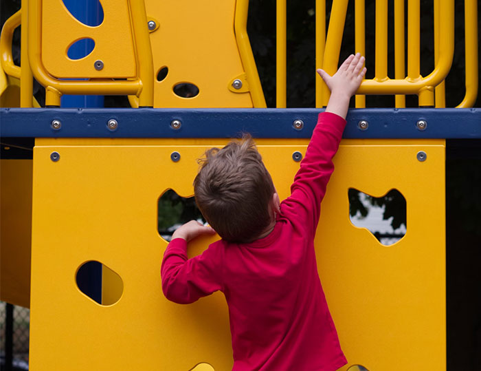 Child in a red shirt reaching up on a yellow playground structure, illustrating coincidences.
