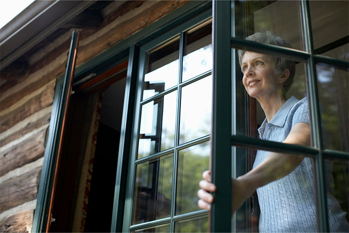Woman in a light blue shirt looking out of a cabin window, surrounded by nature, symbolizing extraordinary coincidences.