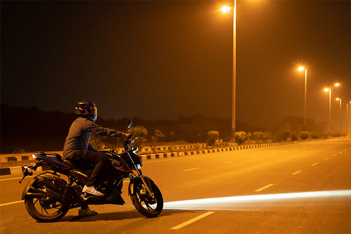 Person on motorcycle at night, headlights on, on an empty street.