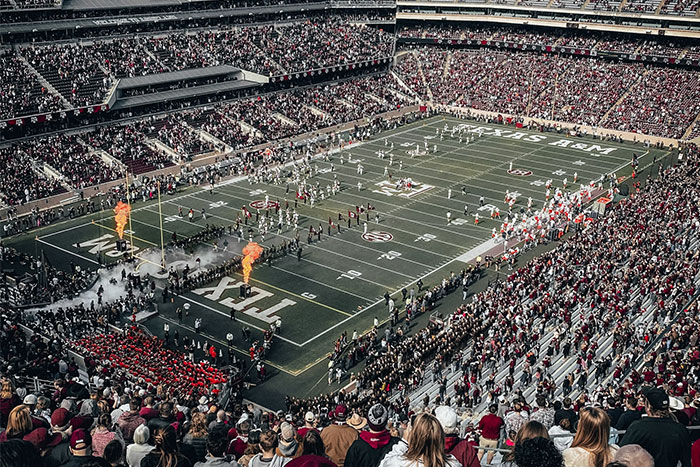 Crowded football stadium captures an amazing coincidence as teams enter the field with lively cheers and pyrotechnics.