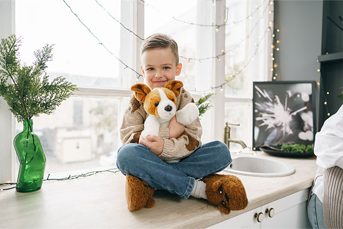Child with a plush dog toy seated by a window, surrounded by fairy lights, embodying a crazy coincidence vibe.
