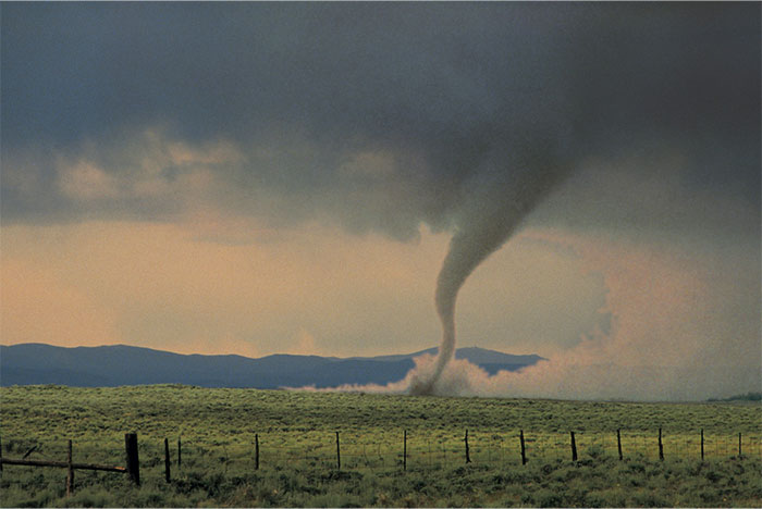 Tornado forming over open field under a cloudy sky, illustrating a remarkable coincidence in nature.