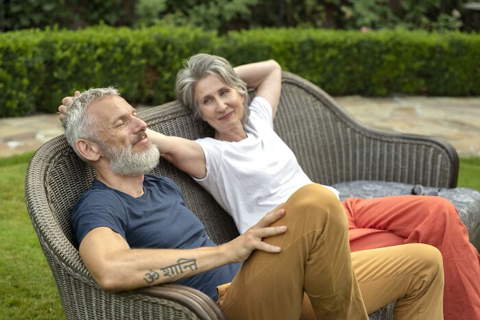 Couple relaxing on a wicker bench in a garden, smiling and enjoying the moment together.