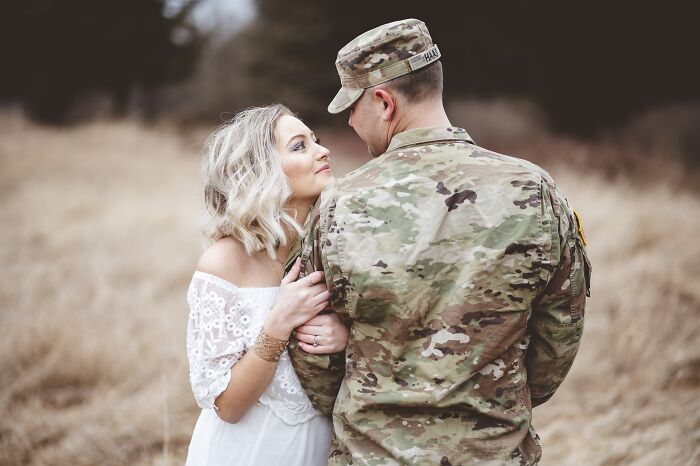 A woman in a white dress embraces her partner in military uniform outdoors, symbolizing stuck hard times together.