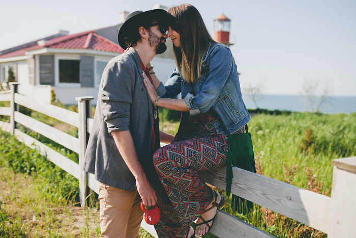 Couple embracing near a fence by a house and lighthouse, symbolizing support during hard times together.
