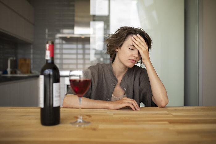 Person looking stressed at a table with a wine bottle and glass, illustrating partners facing hard times.