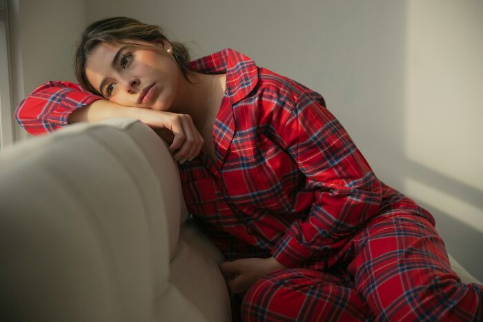 Woman in red plaid pajamas looking thoughtful while resting on a couch, depicting hard times.