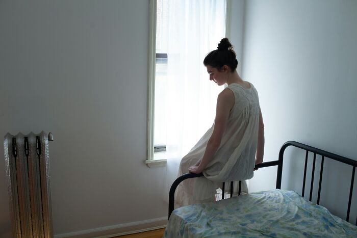 A woman in a white dress sits pensively on a bed, capturing the essence of hard times with partners.