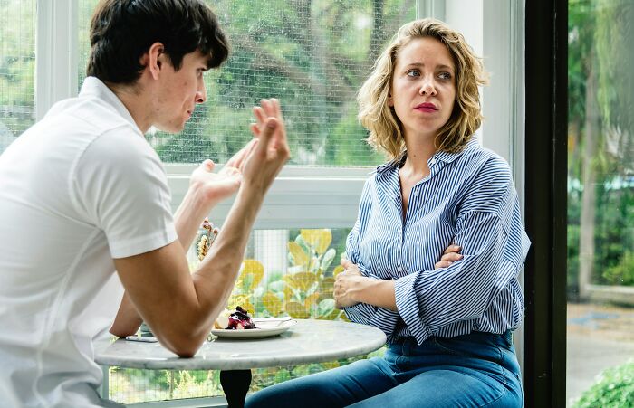 Two partners in discussion at a café, with one looking concerned and crossing arms, illustrating hard times in relationships.