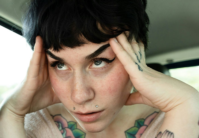 Student looking shocked and distressed in a car, featuring tattoos and piercings.