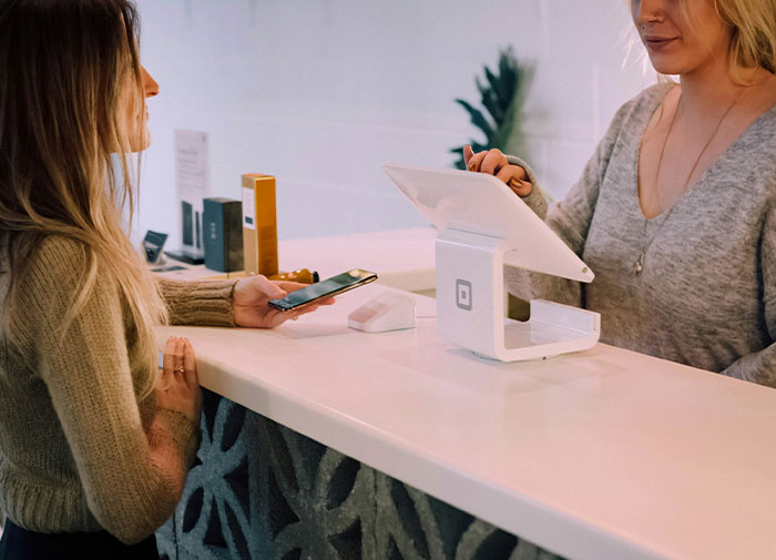 Woman at the counter with a smartphone near a point of sale device.