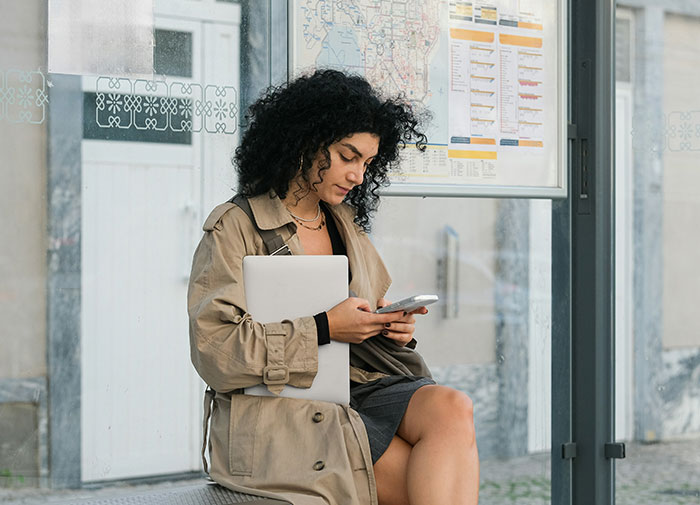 Woman with a laptop and phone at a bus stop, managing her schedule. Woman with a laptop and phone at a bus stop, managing her schedule.