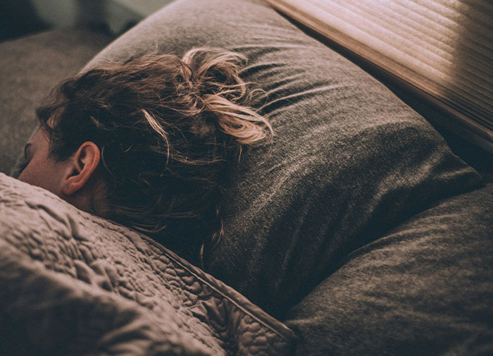 Person resting on a bed, highlighting babysitting and scheduling challenges. Person resting on a bed, highlighting babysitting and scheduling challenges.