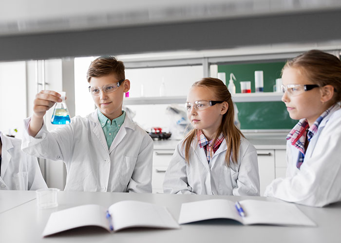 Young students in lab coats, observing a test tube, showcasing one of the stupid things people did despite warnings.