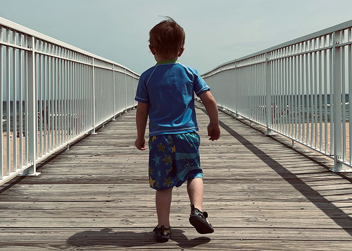 Child walking on a boardwalk towards the beach, wearing a blue outfit with star patterns.