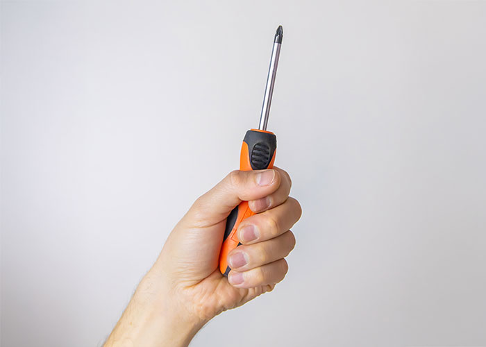 Hand holding an orange screwdriver, illustrating a stupid thing done despite warnings.