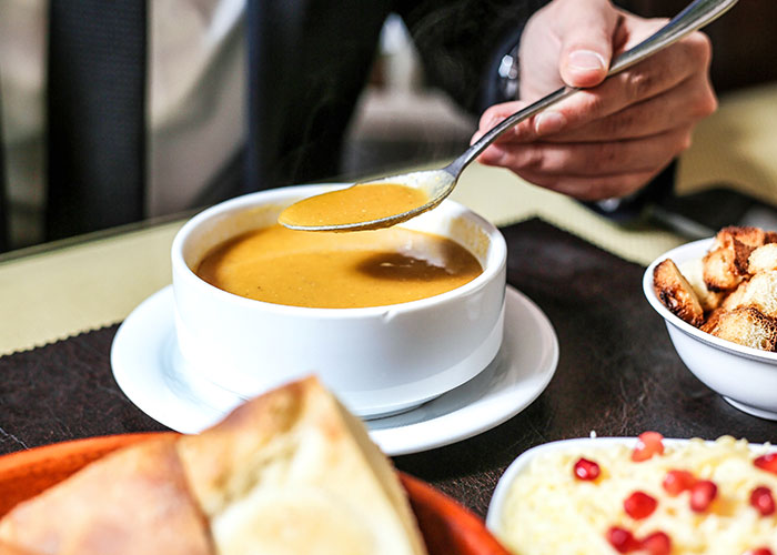 Person eating soup with bread on the side in a restaurant setting, emphasizing a typical dining experience.