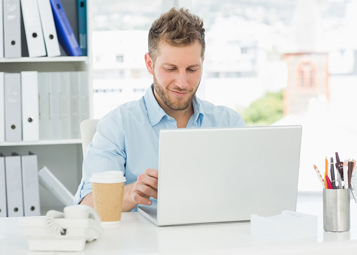 Man working on a laptop in a bright office, ignoring advice, representing stupid things people do.