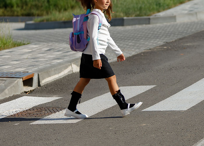 Child walking on a crosswalk with a purple backpack, ignoring safety advice.