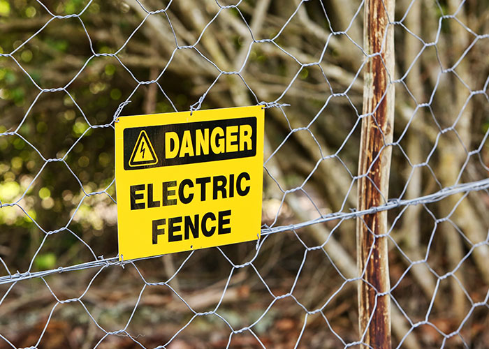 Yellow warning sign on an electric fence indicating danger.