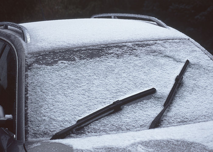 Car windshield covered in snow, with wipers ineffectively positioned; showcasing a common stupid mistake.