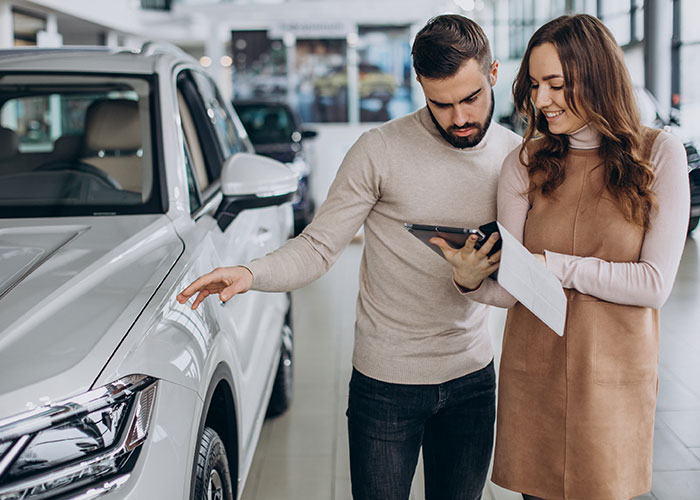 Couple in dealership examining a car and discussing details, possibly ignoring previous advice on vehicle purchase options.